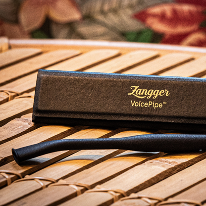 The black Zangger VoicePipe vocal warm-up tube beside its case on a wooden slatted surface